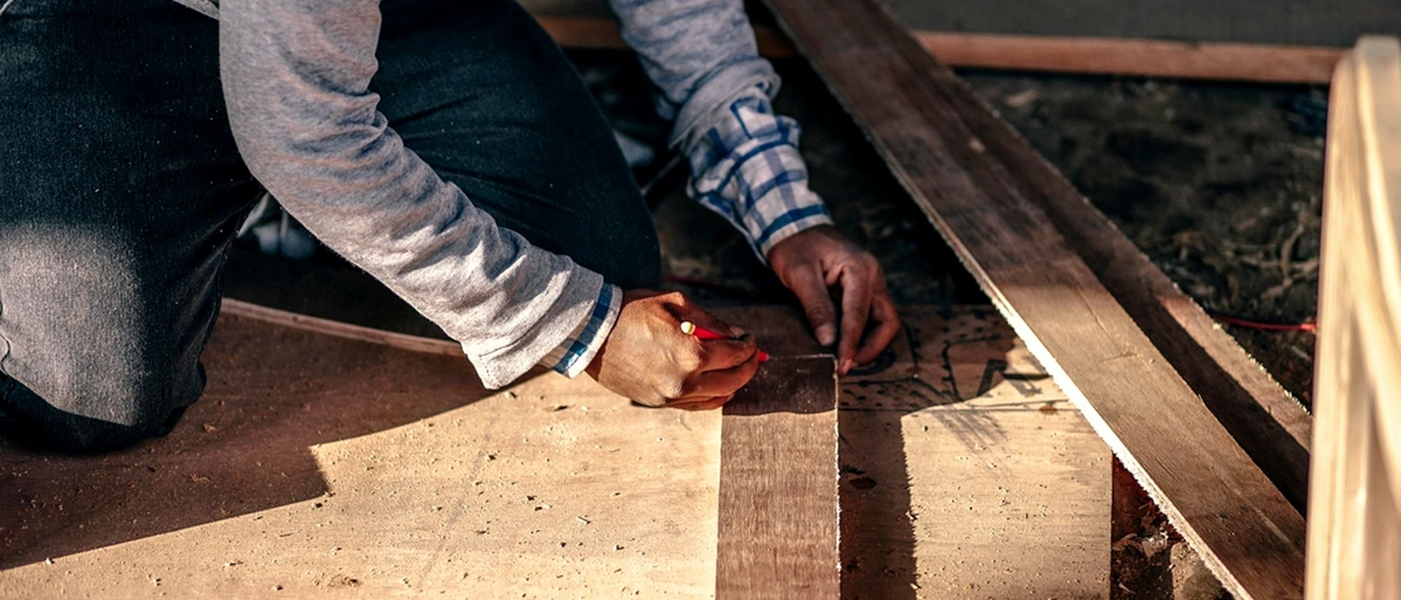 A tradesperson kneeling to mark a length of timber before cutting it.