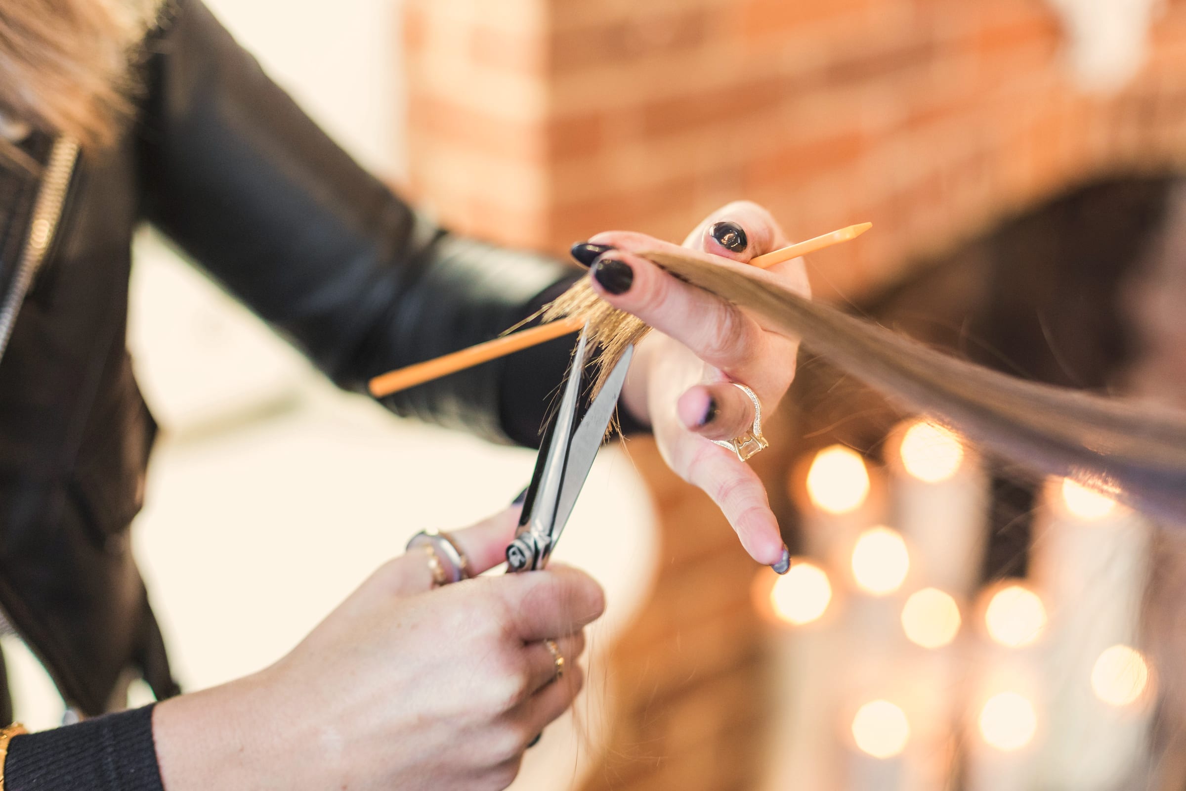 A stylist's hands holding shears and a lock of hair, the salon lights soft behind.